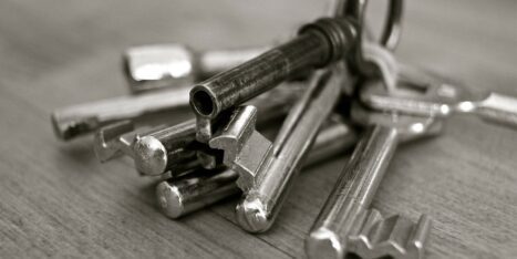 A close-up, black and white photo of an assortment of metal keys on a wooden surface.
