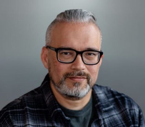 Adult man with glasses and a plaid shirt, posing for a portrait.