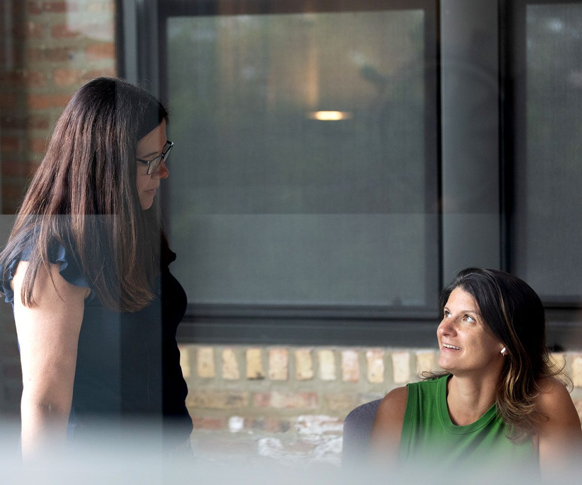 Orbiteers, Stephanie and Mari seen through a window having a discusson
