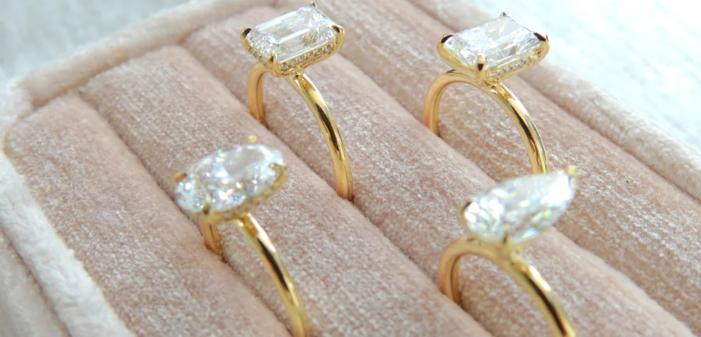 Three diamond engagement rings with gold bands displayed in a velvet-lined box.