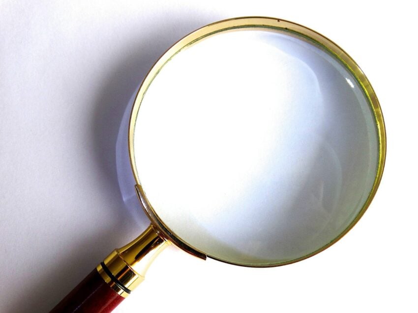 A magnifying glass with a wooden handle and gold rim lying on a white surface.