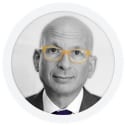 A bald man with glasses wearing a suit and tie, photographed against a plain background.