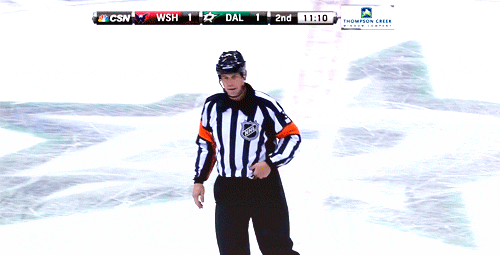 Hockey referee signaling a penalty during a washington vs. dallas game, while skating across the ice.