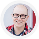 Man wearing glasses and a red plaid shirt, smiling at the camera.