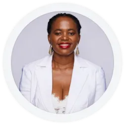 A woman wearing a white blazer and earrings, with braided hair and red lipstick, poses in front of a plain light background.