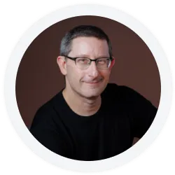 A middle-aged man with short gray hair and glasses is smiling slightly, wearing a black shirt, against a plain dark background.
